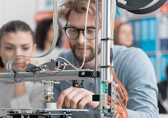 Engineering students using a 3D printer in a lab