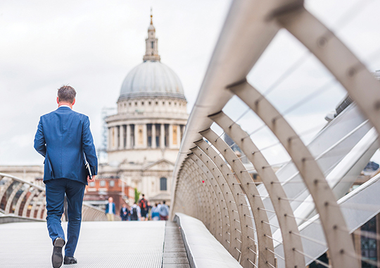 Businessman walking across a bridge in London, England, with St. Paul’s Cathedral in the distance