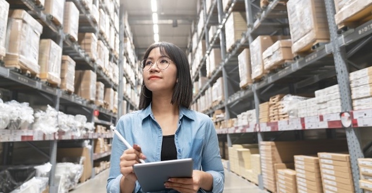 Young asian woman auditor in a warehouse looking up stock taking inventory on a computer tablet